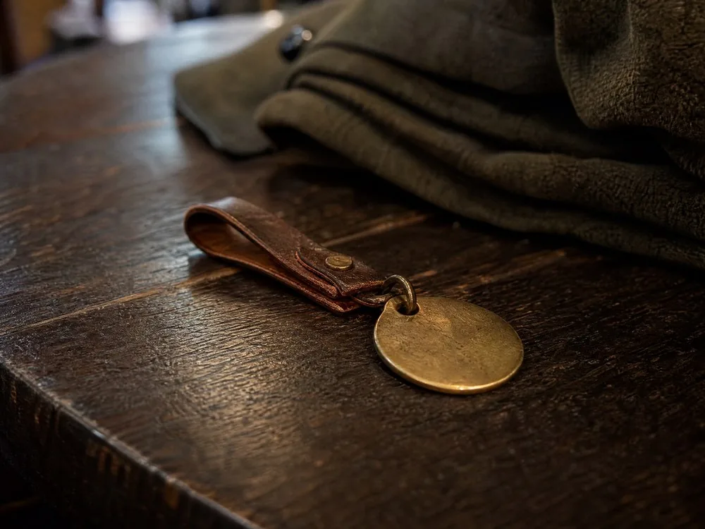 Une étiquette en laiton pour vestiaire sur une boucle en cuir à côté d'un manteau plié