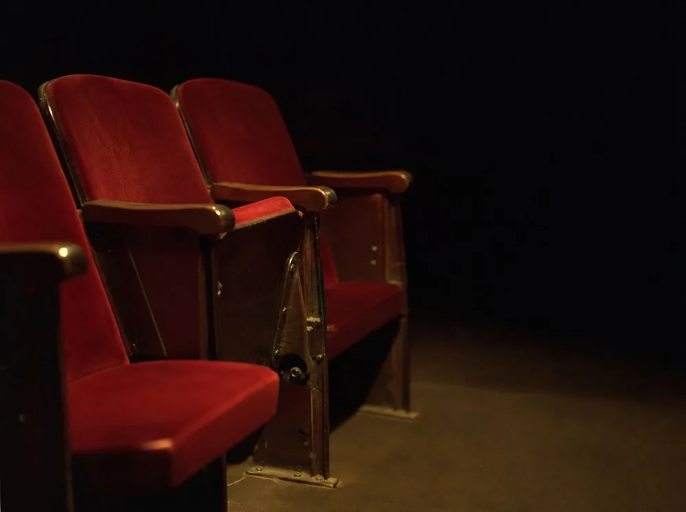 Une courte rangée de sièges en velours rouge vides dans un auditorium sombre